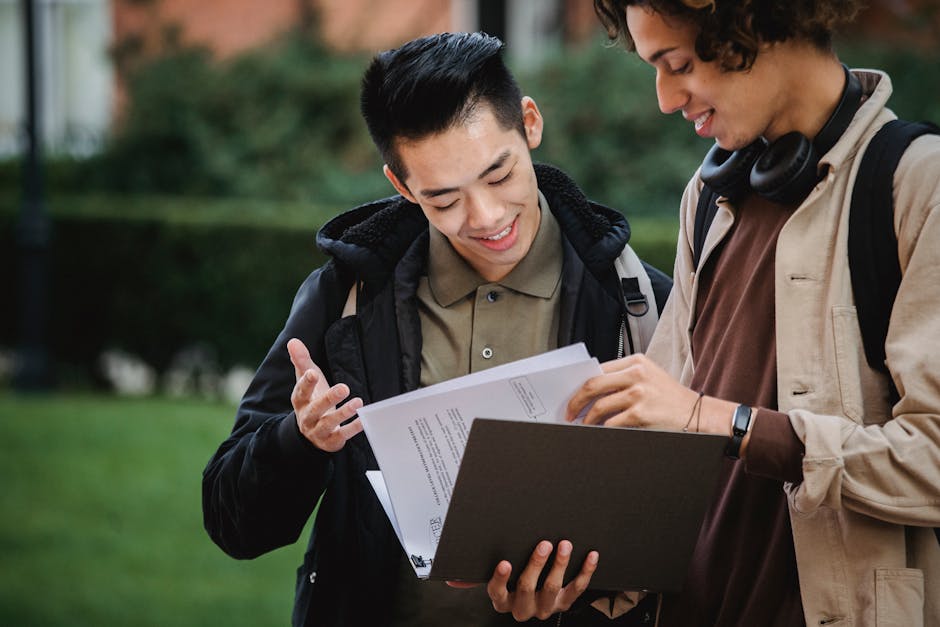 Two students discussing a document outdoors on campus, engaged in a collaborative academic project.