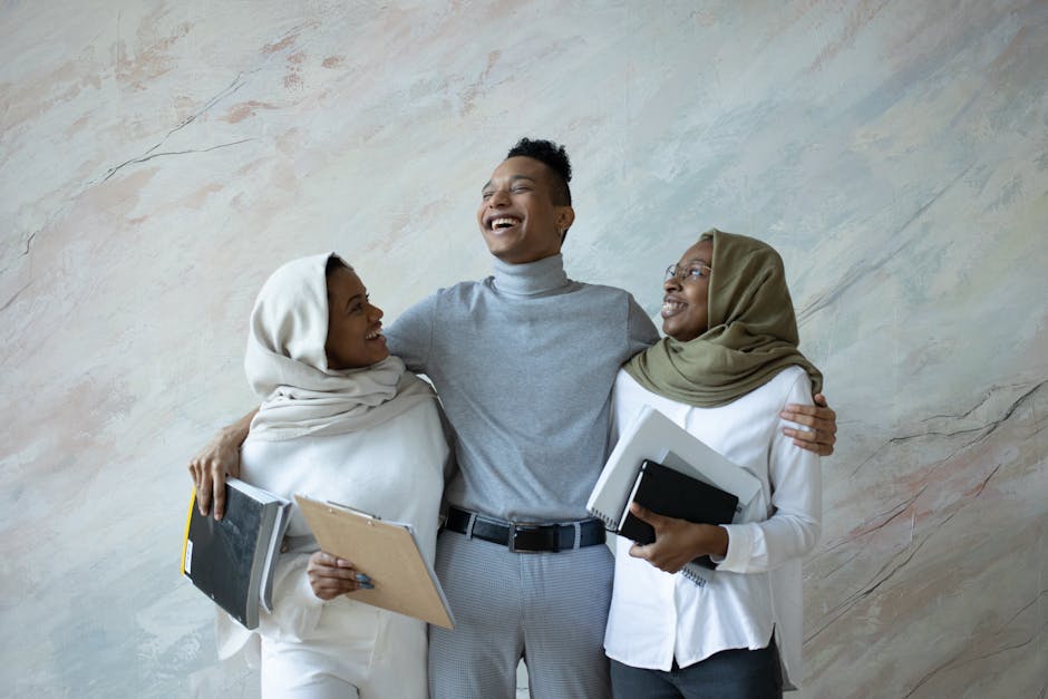 Team of African American classmates with documents and notepad hugging each other and laughing joyfully
