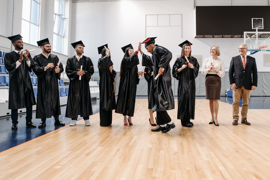 Students and faculty celebrating graduation with high fives in a sports hall.