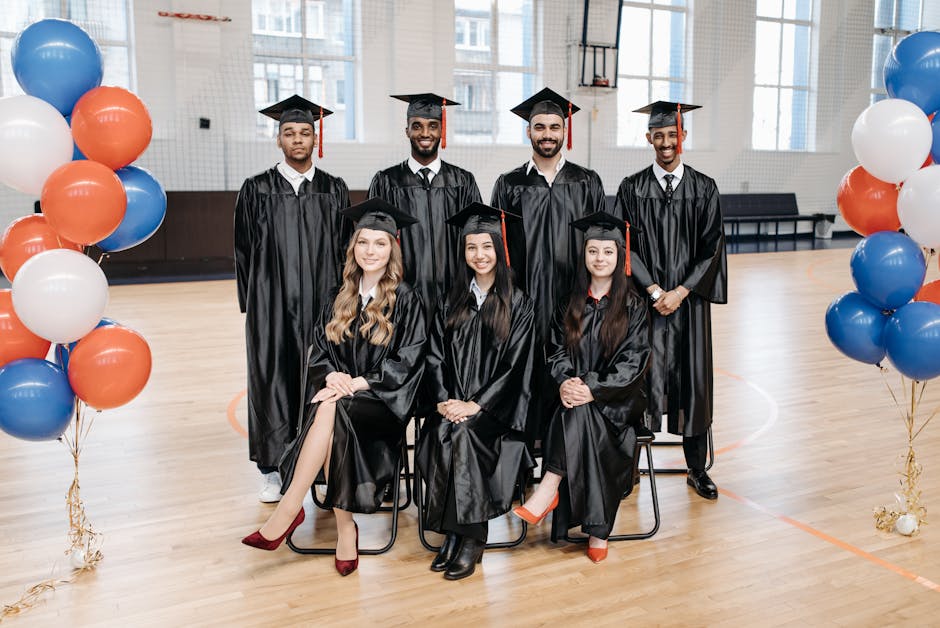 Diverse group of graduates in gowns and caps posing indoors with balloons.