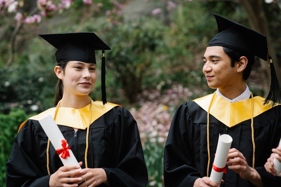 Two young graduates with diplomas celebrate their achievement in graduation caps outdoors.