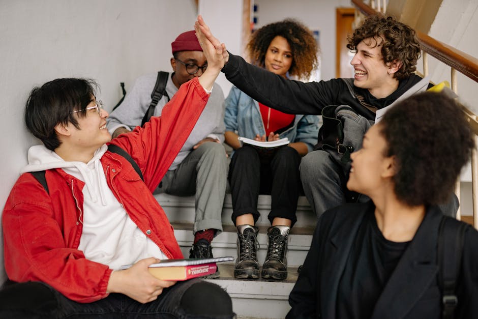 A diverse group of happy students sitting on a staircase, high-fiving and smiling.