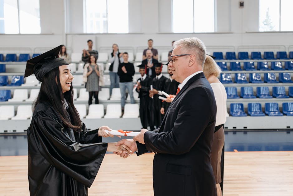 A proud graduate receiving diploma from teacher in a gymnasium amidst applause, capturing a moment of achievement.