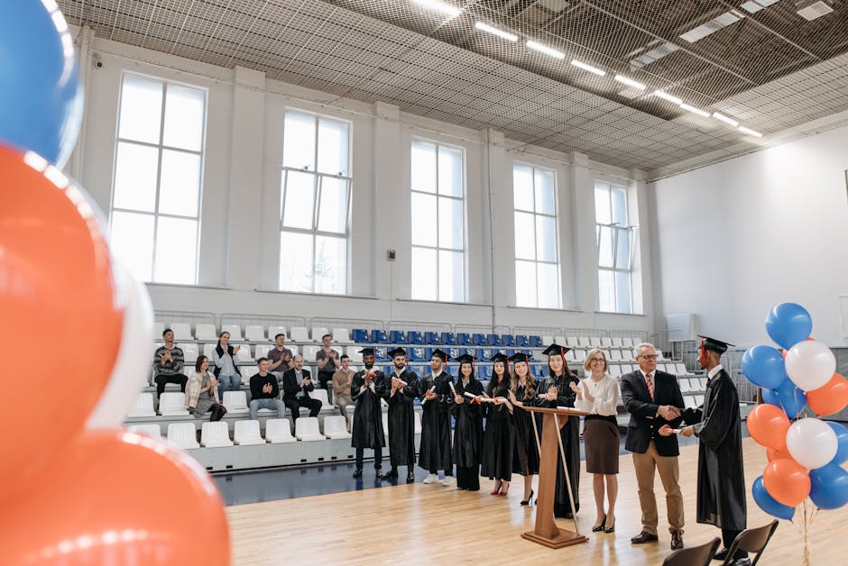 Graduates receiving diplomas indoors with audience. Academic success celebrated.