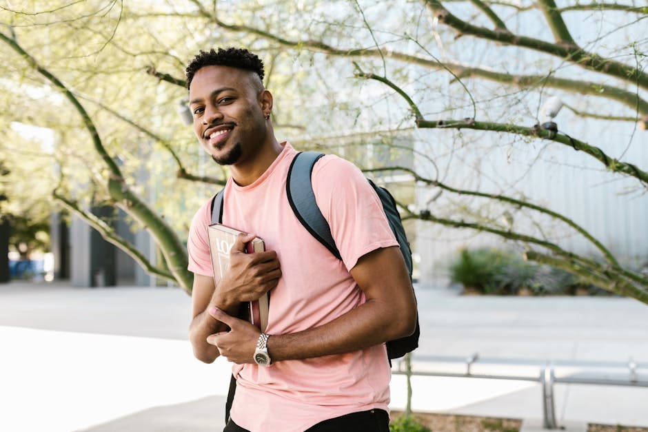 Smiling young African American man with a backpack and book at a college campus.
