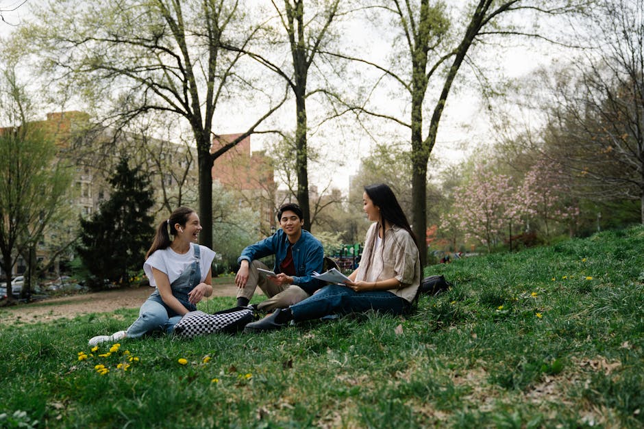Group of college students sitting and chatting on the grass in a park during spring.