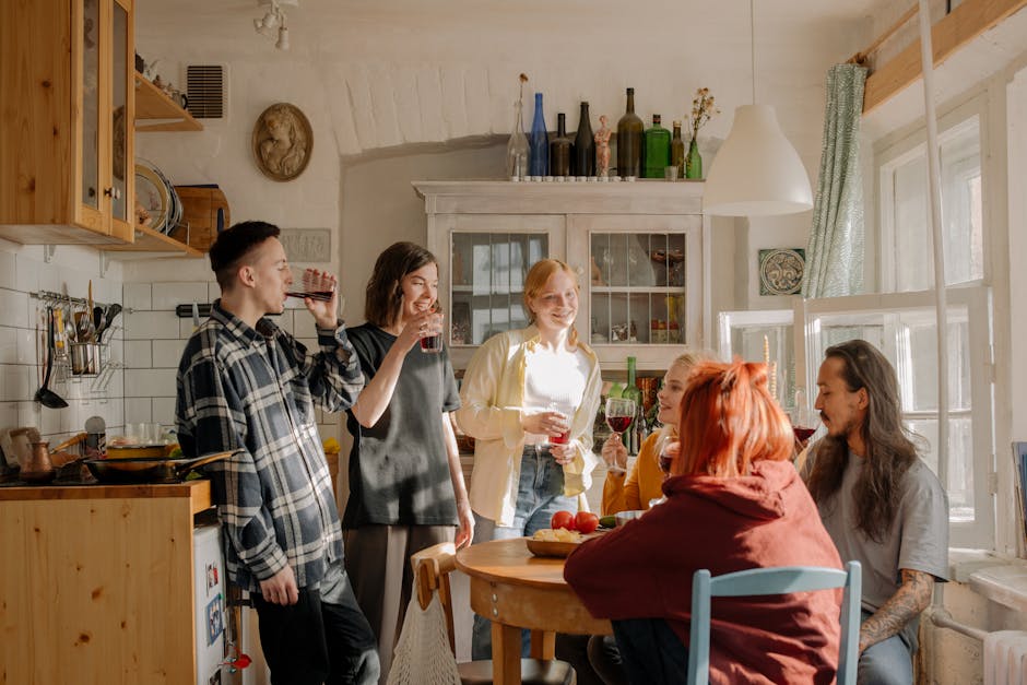 A group of friends laughing and enjoying drinks in a cozy kitchen setting.