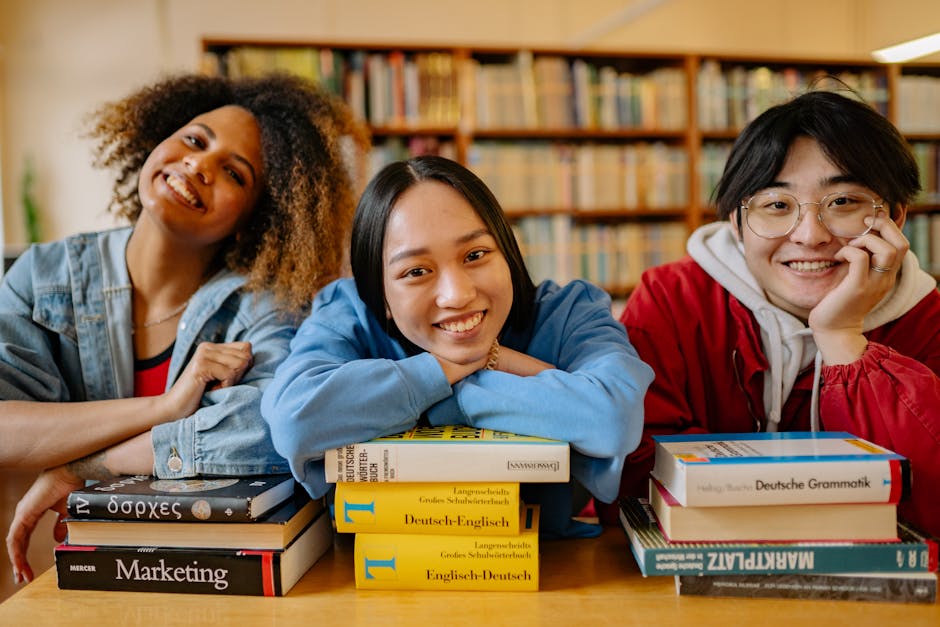 Three smiling students in a library, engaged in studying with stacks of books.