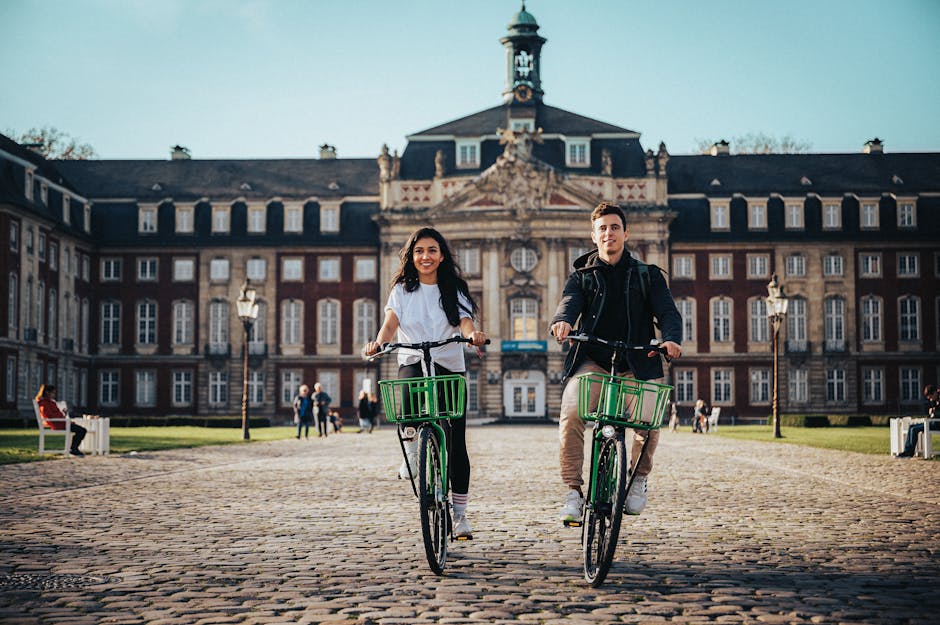 A couple rides bicycles in front of the University of Münster on a sunny day.