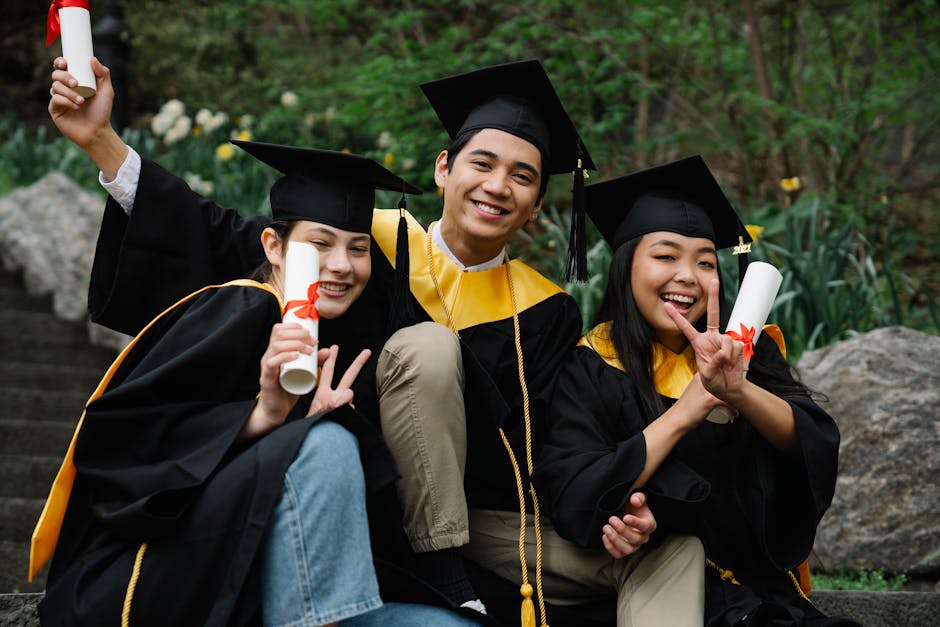 Three college graduates in caps and gowns celebrating success outdoors with diplomas.