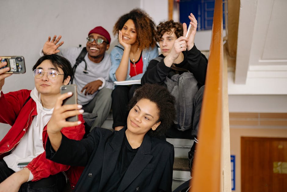A diverse group of smiling students taking selfies indoors, capturing moments together.