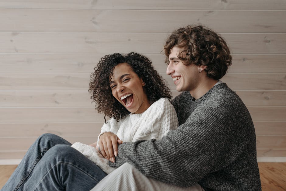 Happy couple laughing together indoors, wearing cozy sweaters. A warm and affectionate moment captured.