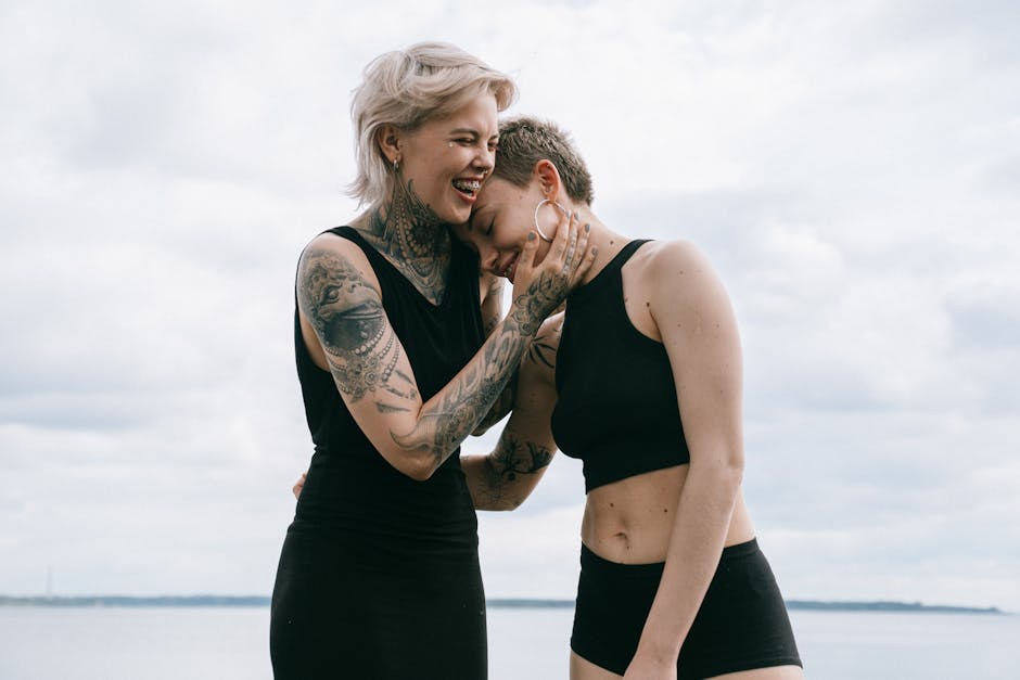 A happy lesbian couple in black attire laughing together on a beach, showcasing love and friendship.