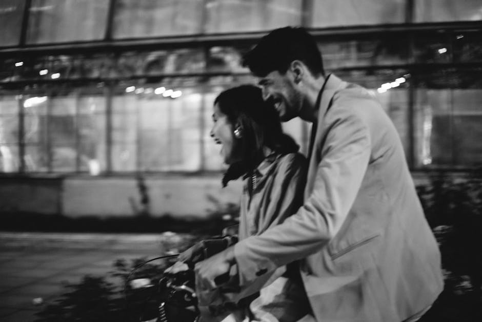 A couple enjoys a joyful evening bike ride in a romantic black and white setting.