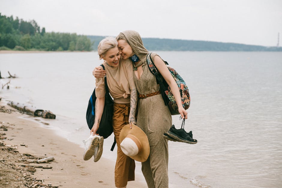 Two friends enjoy a joyful walk along the beach, embracing and smiling.