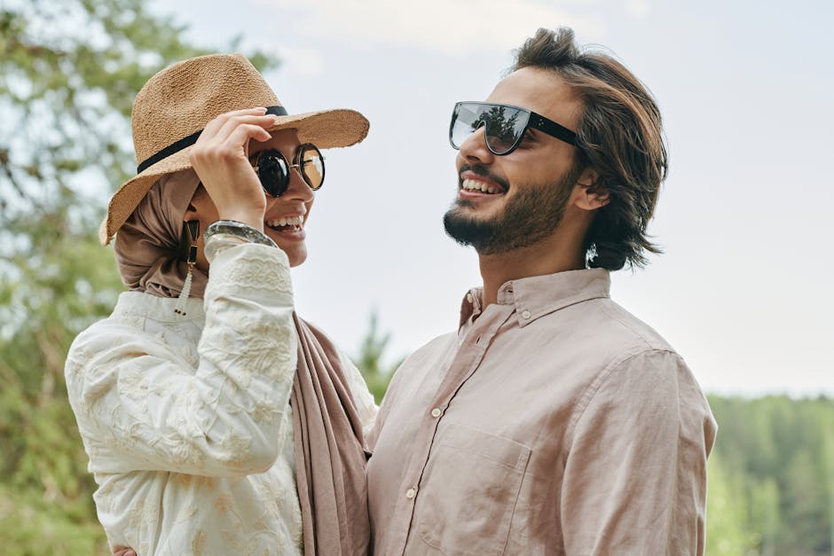 A joyful couple wearing sunglasses and hats, smiling under a bright summer sky.