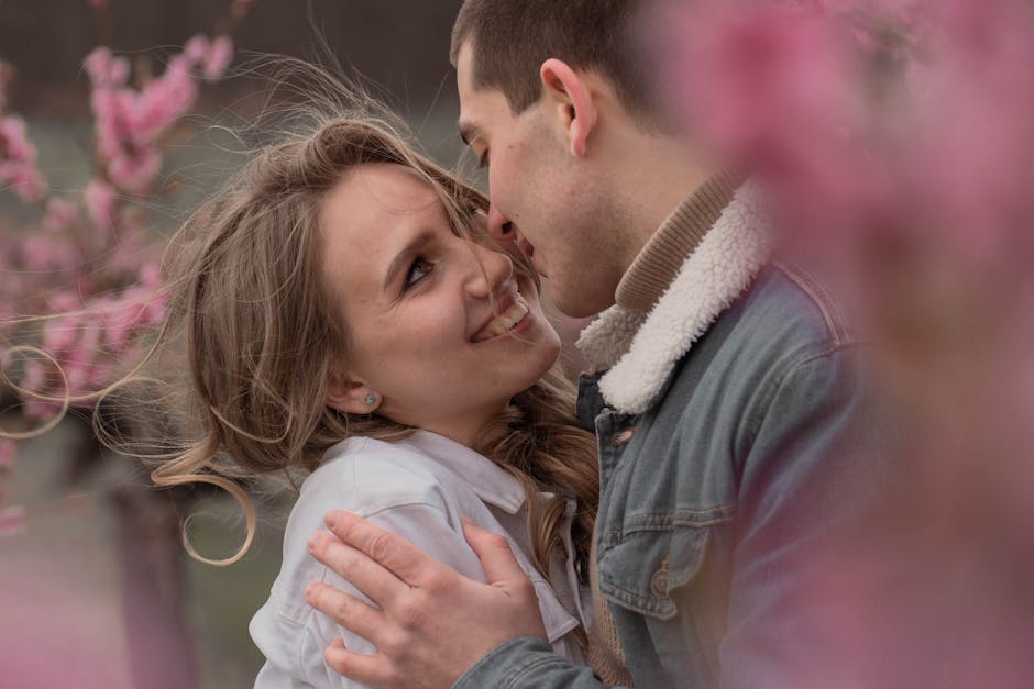 Happy couple embracing in a field with pink spring flowers, exuding love and joy.