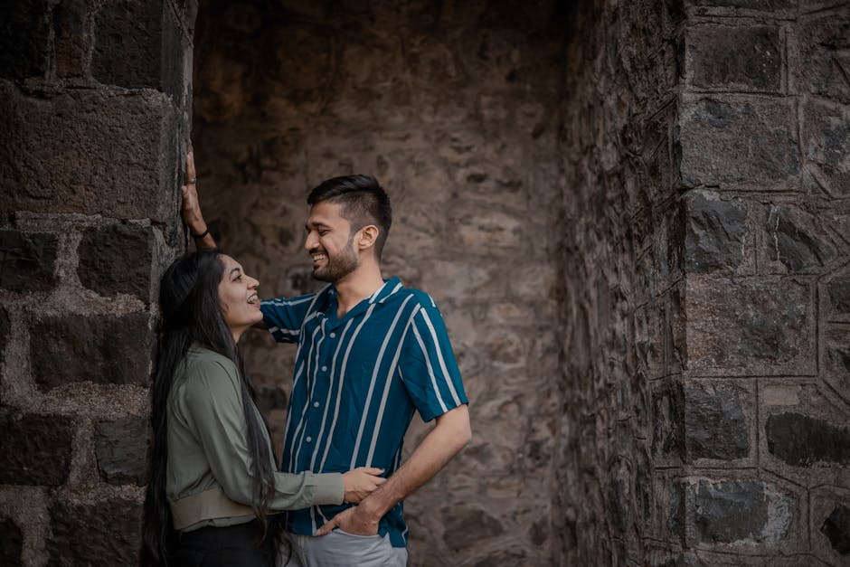 A joyful couple sharing a laugh while leaning on a rustic stone wall, capturing an intimate and playful moment outdoors.