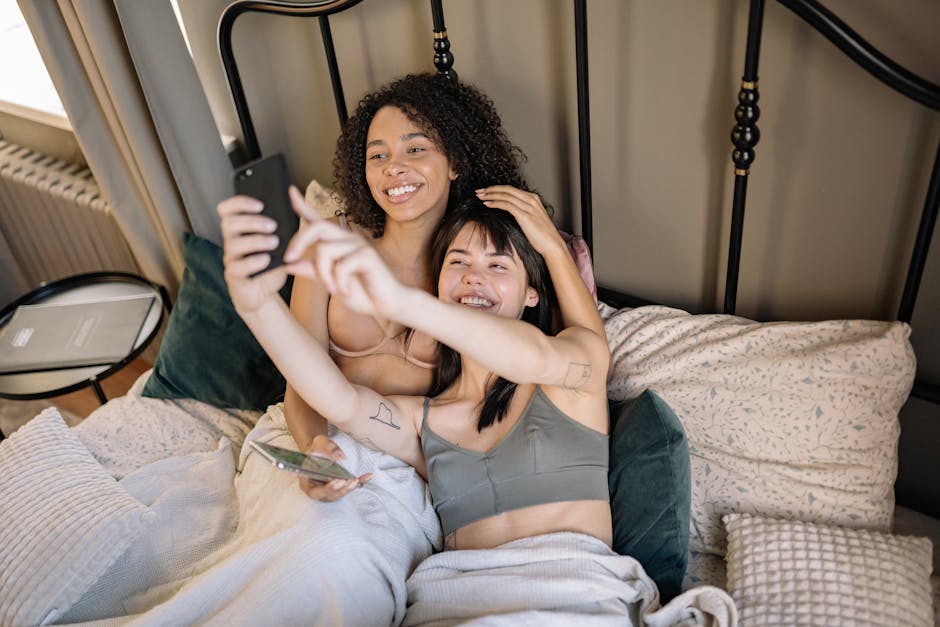 Joyful couple lying in bed, capturing a selfie with a smartphone, full of love and laughter.