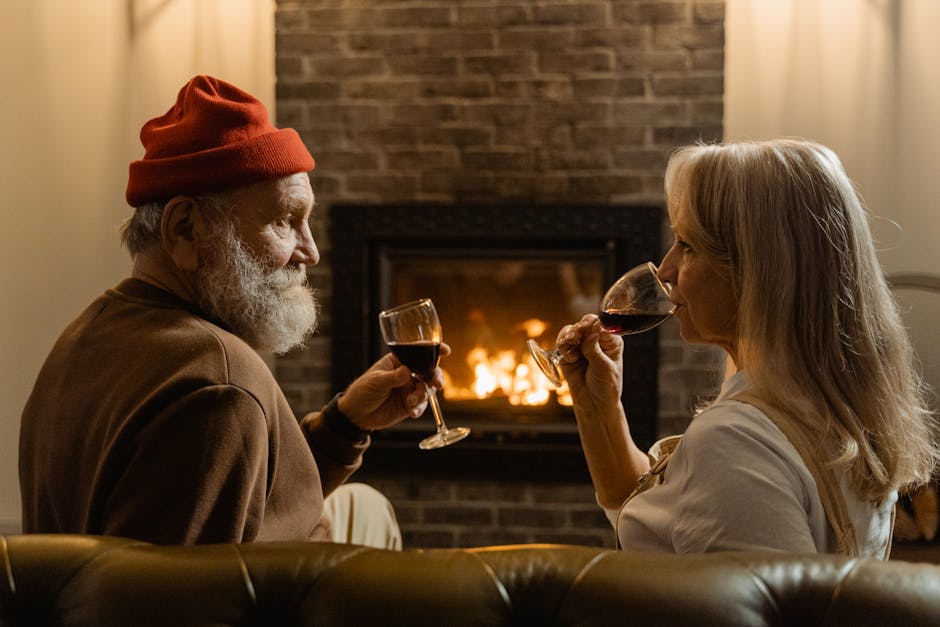 A senior couple relaxes at home, savoring wine by the cozy fireplace.