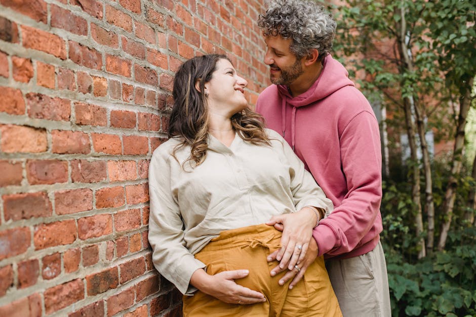 A joyful couple embracing while expecting a baby, standing by a brick wall outdoors.