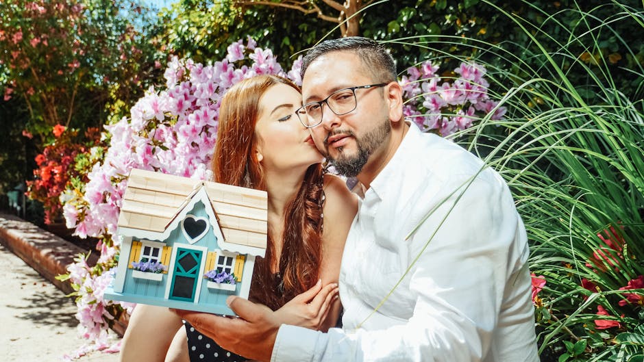 Happy couple with a miniature house model, symbolizing new home purchase, in a vibrant garden.