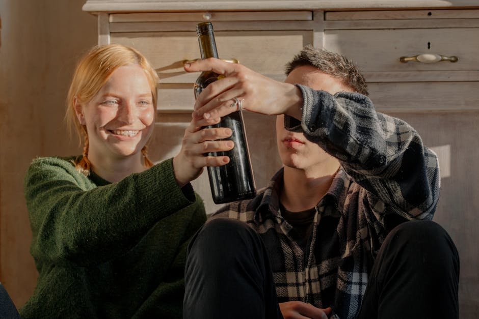 Laughing couple holding a wine bottle, enjoying a cozy indoor moment.