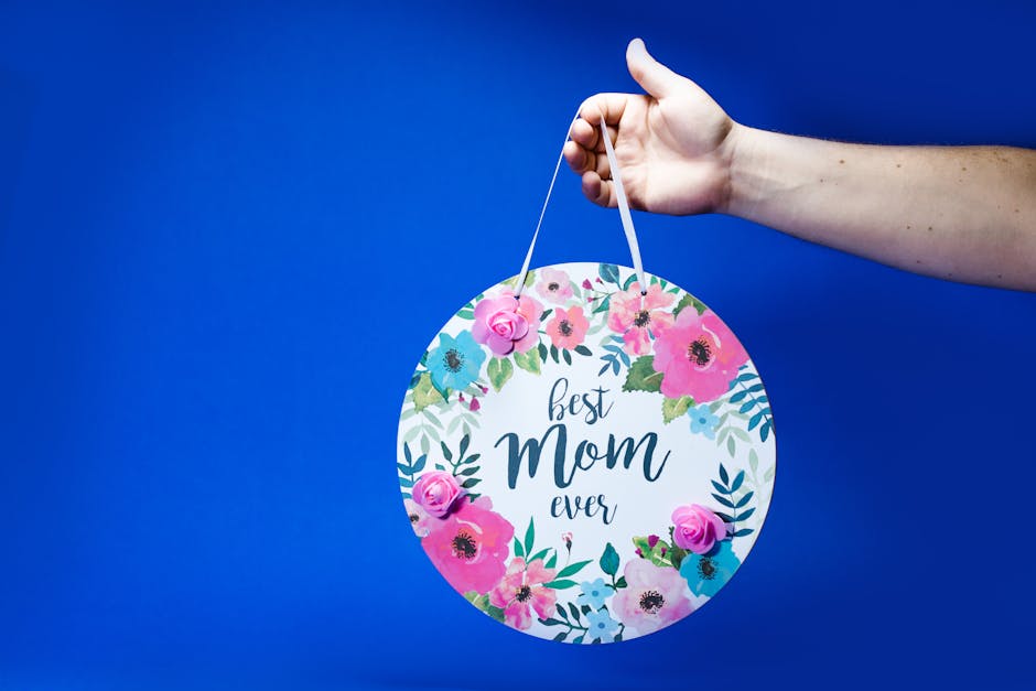 A cheerful floral Mother's Day sign held in hand against a vibrant blue backdrop.