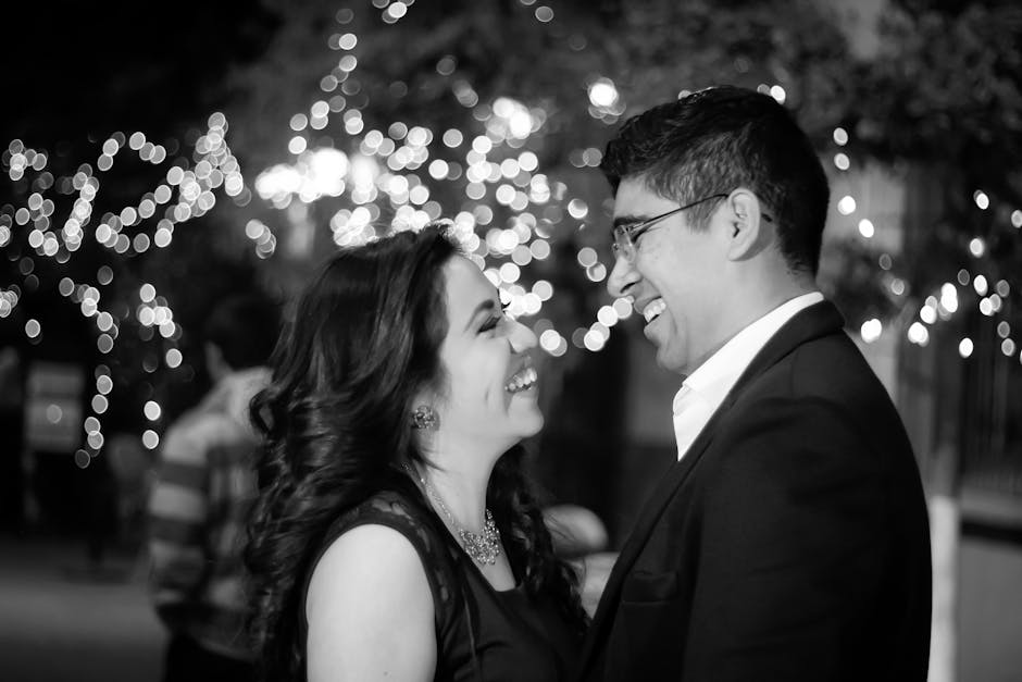 A joyful couple smiling and enjoying a night out with sparkling fairy lights in the background.