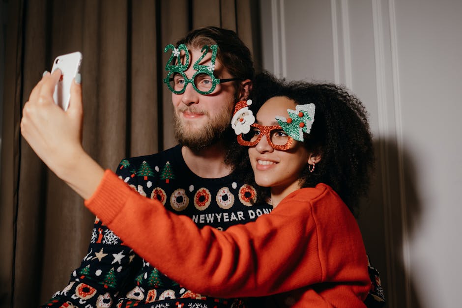 A joyful couple takes a selfie during New Year's celebration, wearing festive glasses and sweaters.