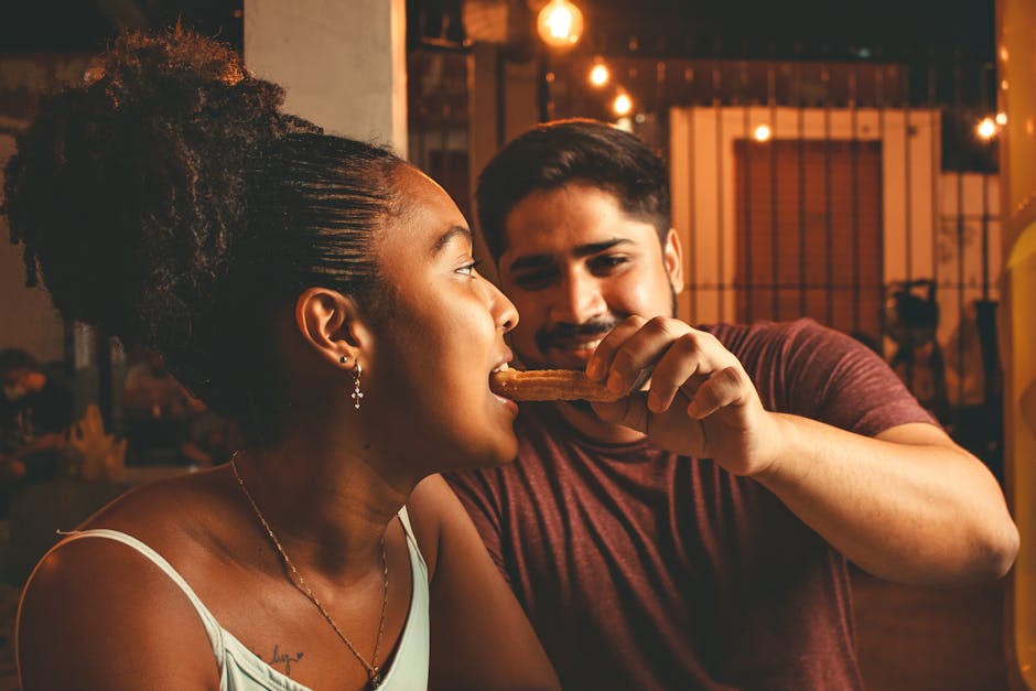 A couple enjoying a night out, sharing a churro under warm lights, expressing love and joy.