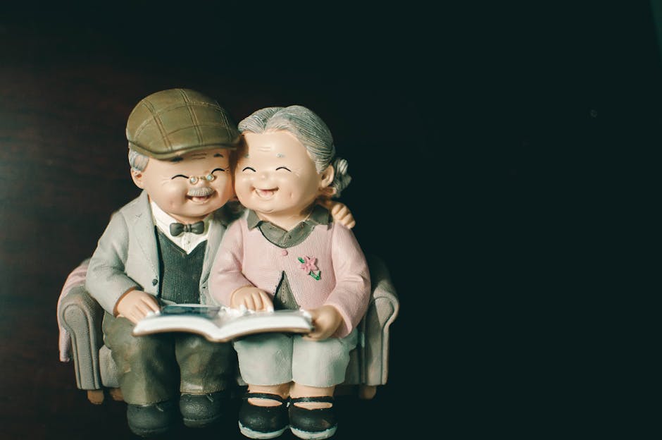 Cute figurines of an elderly couple sitting on a sofa and sharing a book, evoking warmth and nostalgia.
