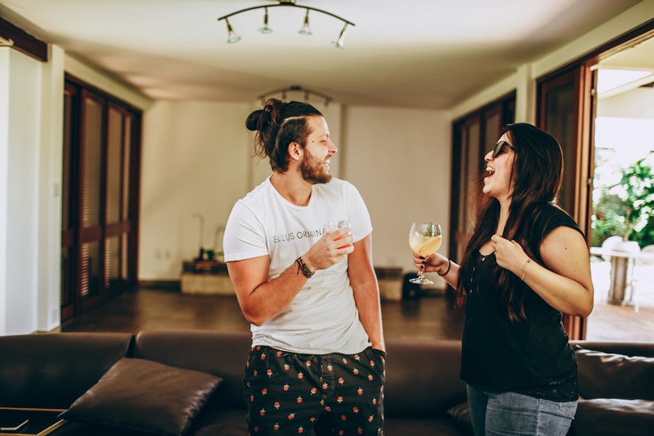 Young man and woman in casual outfit smiling and looking at each other while having fun at home during romantic meeting on daytime