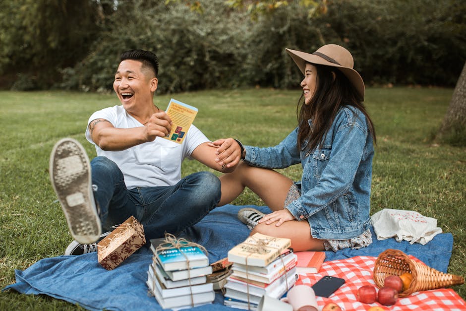 Smiling couple enjoying a lively picnic with books in a sunny park.