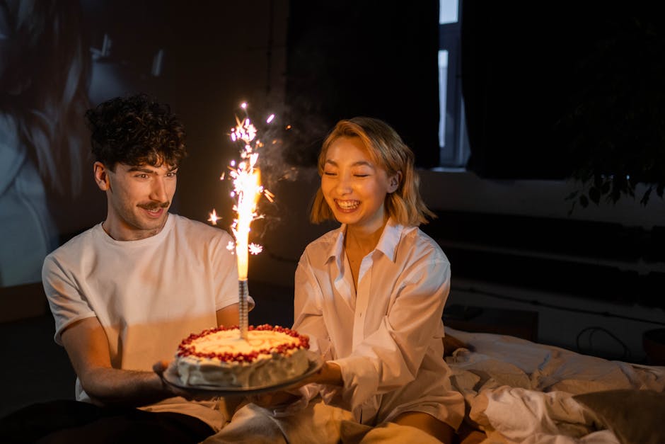 A couple shares a joyful moment with a lit birthday cake indoors.