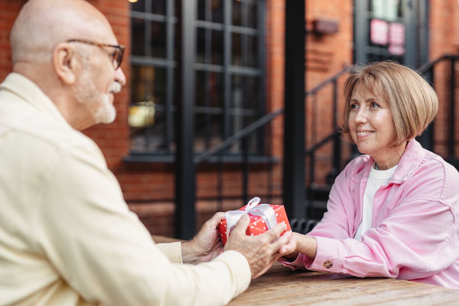 A senior couple shares a touching moment by exchanging a wrapped gift outdoors.
