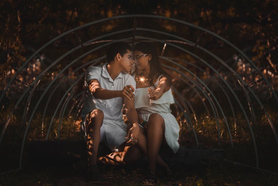 A loving couple sits closely under an arch, holding a sparkler, sharing an intimate moment.