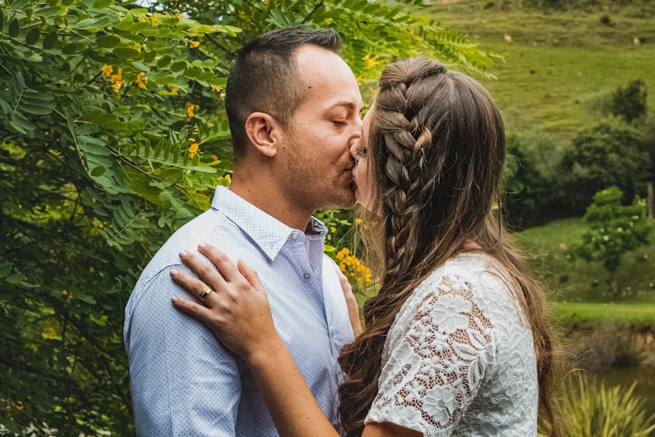 A romantic moment captured as a couple kisses in a lush outdoor setting.