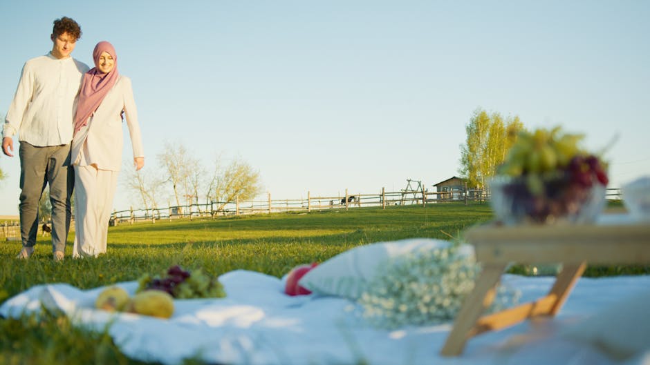 A couple enjoys a serene walk near a picnic setup in a sunny grass field.