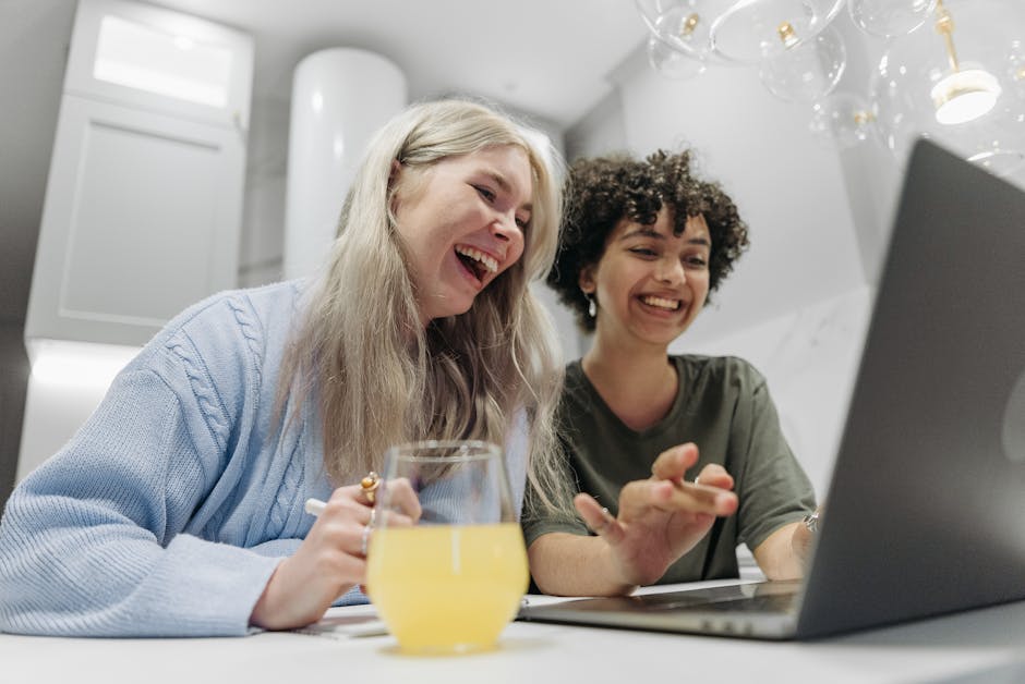 A joyful LGBTQ couple laughing while using a laptop indoors, enjoying a beverage.