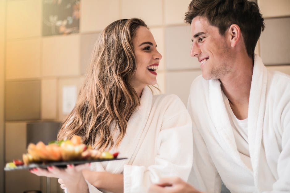 Side view of content couple in bathrobes relaxing on bed with platter of mixed fruit and looking at each other