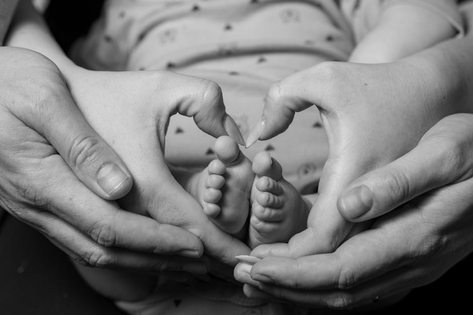 Close-up of adult hands forming heart shape around a baby's feet, symbolizing love and care.