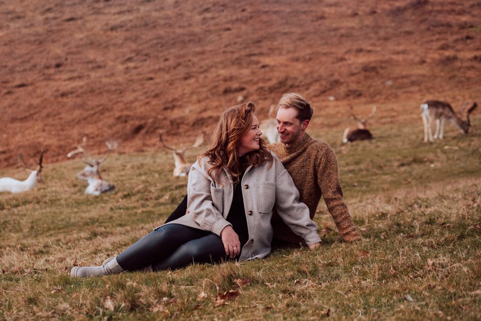 Happy couple sitting in a grassy field with deer in rural Leicester, England.