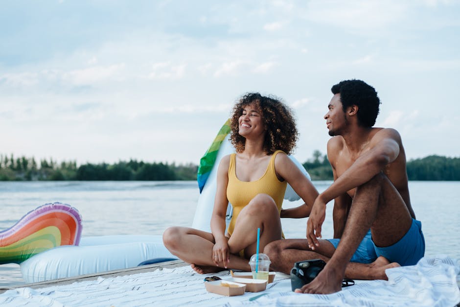 Joyful couple enjoying a summer picnic by the lake with swimsuits, laughter, and a beautiful view.
