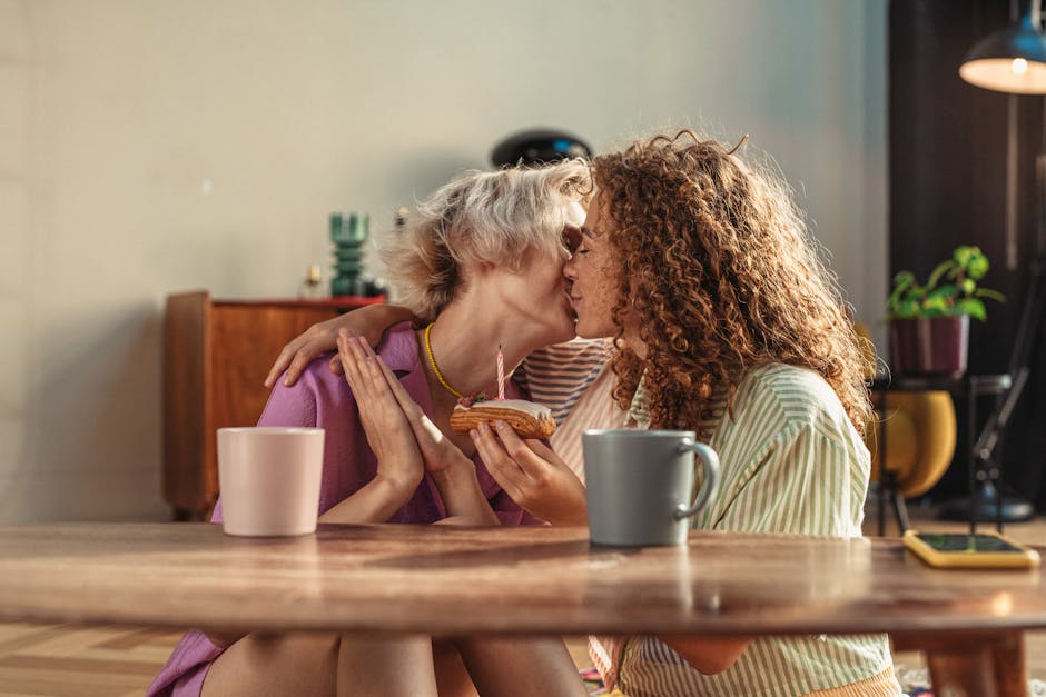 A loving couple shares a kiss while celebrating with a cupcake in a cozy indoor setting.