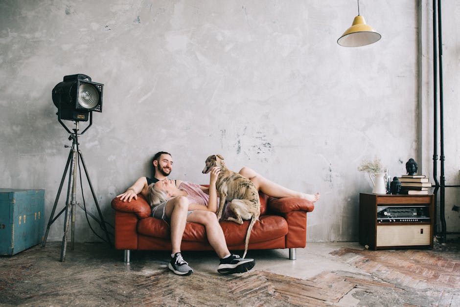 A bearded man smiling on a leather couch with a dog in a stylish industrial setting.