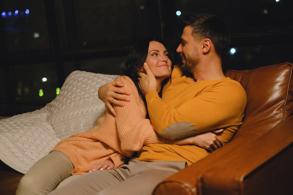 A loving couple embracing and smiling while relaxing on a sofa indoors, creating a warm and intimate atmosphere.