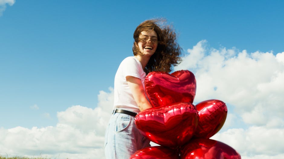 A young woman enjoys a windy day outdoors with a bundle of red heart-shaped balloons.
