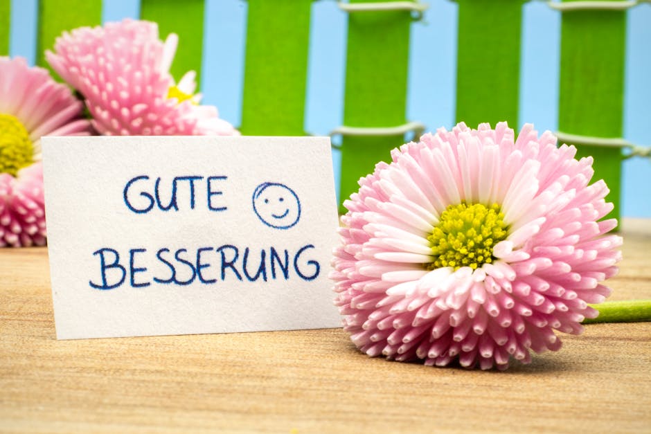 Pink daisies beside a heartfelt 'Gute Besserung' card on wooden table.
