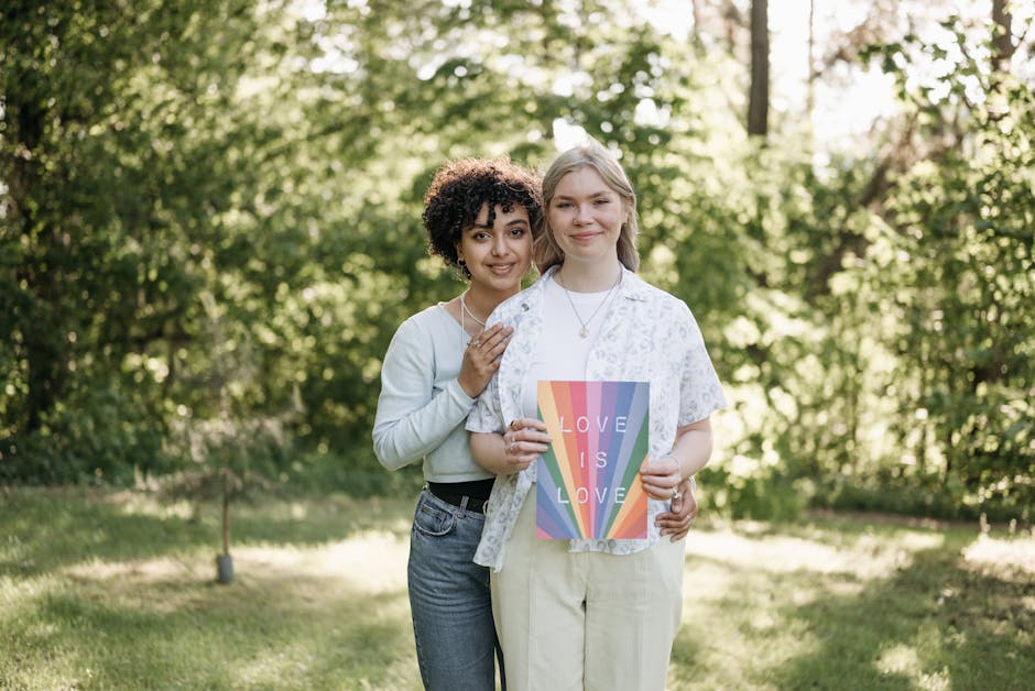 Two women holding a 'Love is Love' rainbow poster in a sunlit park, symbolizing LGBT pride and love.